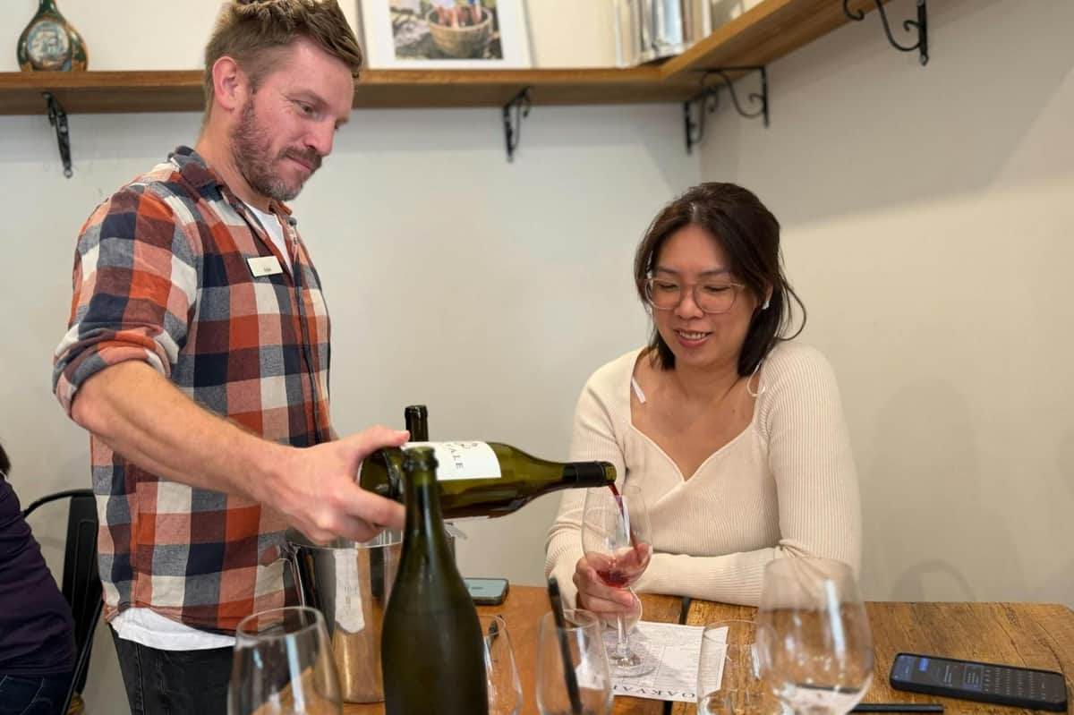 Hunter Valley: Guided Day Trip from Sydney with Tastings + Lunch A man pours wine for a woman seated at a table with wine glasses and a tasting sheet in a cozy setting.