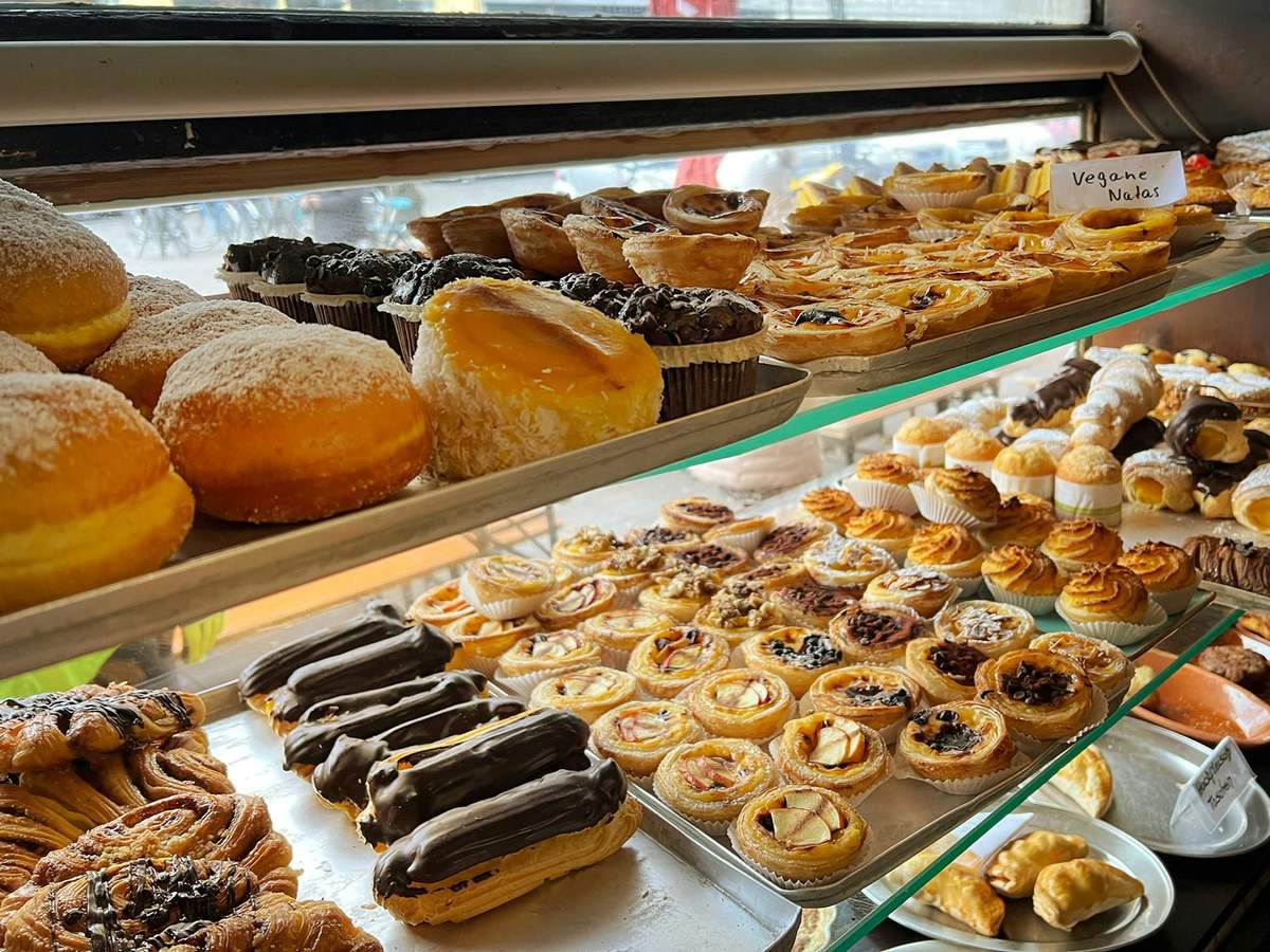 Hamburg: Sternschanze Food Tour A variety of pastries including eclairs, tarts, and donuts displayed on metal and glass shelves in a bakery.
