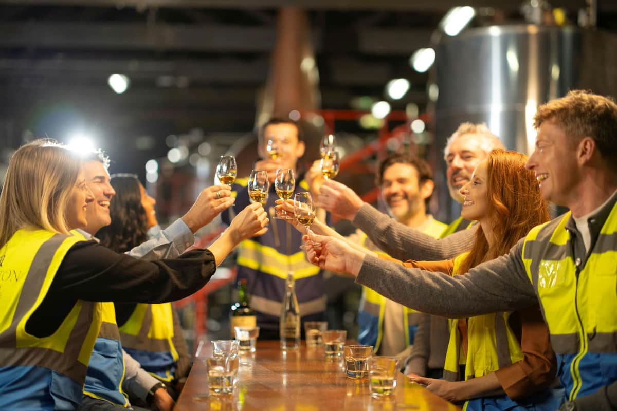 Midleton Distillery (Jameson): Behind-the-Scenes Guided Tour A group of people in safety vests clinking glasses together in a celebratory toast, standing around a wooden table indoors.