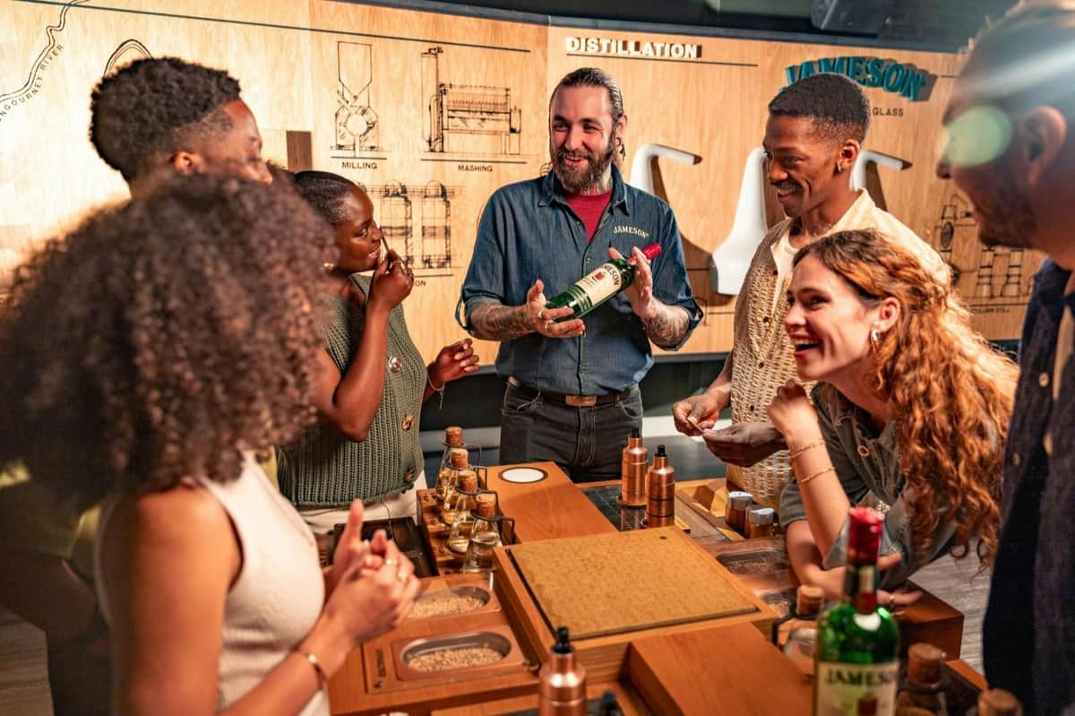 Jameson Distillery: Guided Tour with Tasting A group of people enjoying a whiskey-tasting session at a distillery, with a presenter holding a bottle of Jameson.