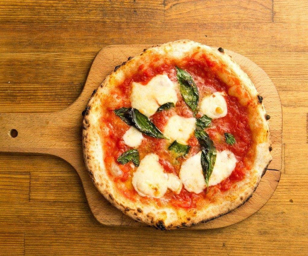Naples: Pizza Tasting + City Center Walking Tour A margherita pizza on a wooden paddle, topped with tomato sauce, melted mozzarella, and fresh basil leaves.