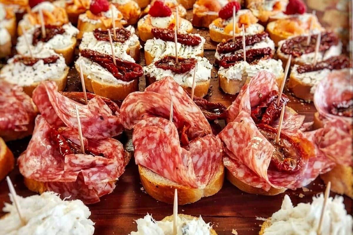 Primer plano de varios aperitivos en pequeñas rebanadas de pan, cubiertos con carnes, quesos, tomates secos y guarniciones.