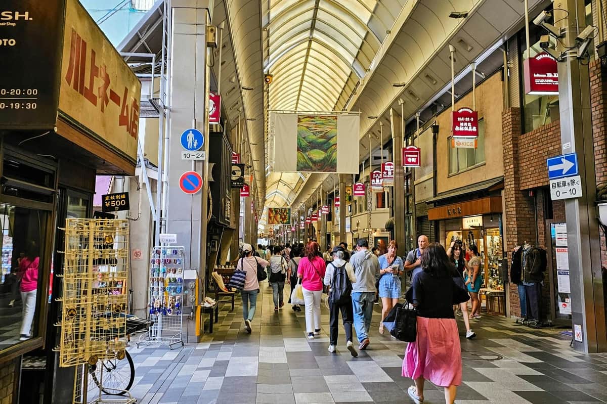 Un marché intérieur bondé avec des gens qui marchent, des boutiques des deux côtés, des lanternes suspendues et un haut plafond voûté.