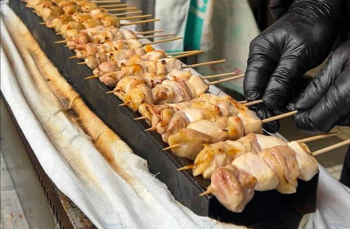 Osaka Dotombori: Food & Local Izakaya Bar Crawl Tour - 3-Hr Tour A person wearing a black glove adjusts skewers of grilled chicken on a rectangular grill with a white cloth underneath.