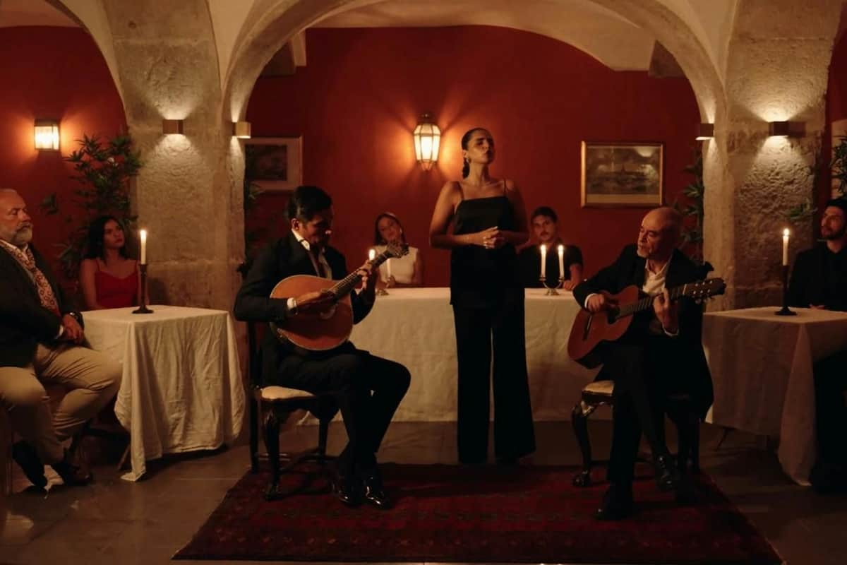 Lisboa: Espectáculo de Fado en Lisboa em Fado + Vino de Oporto (Lisboa) Una actuación en directo en una sala con poca luz, en la que un hombre toca un instrumento de cuerda y una mujer canta, rodeados de invitados sentados.