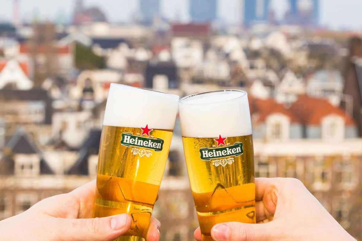 Heineken Experience: Rooftop Bar + 2 Drinks Two glasses of Heineken beer being clinked together, with a blurred urban cityscape in the background.