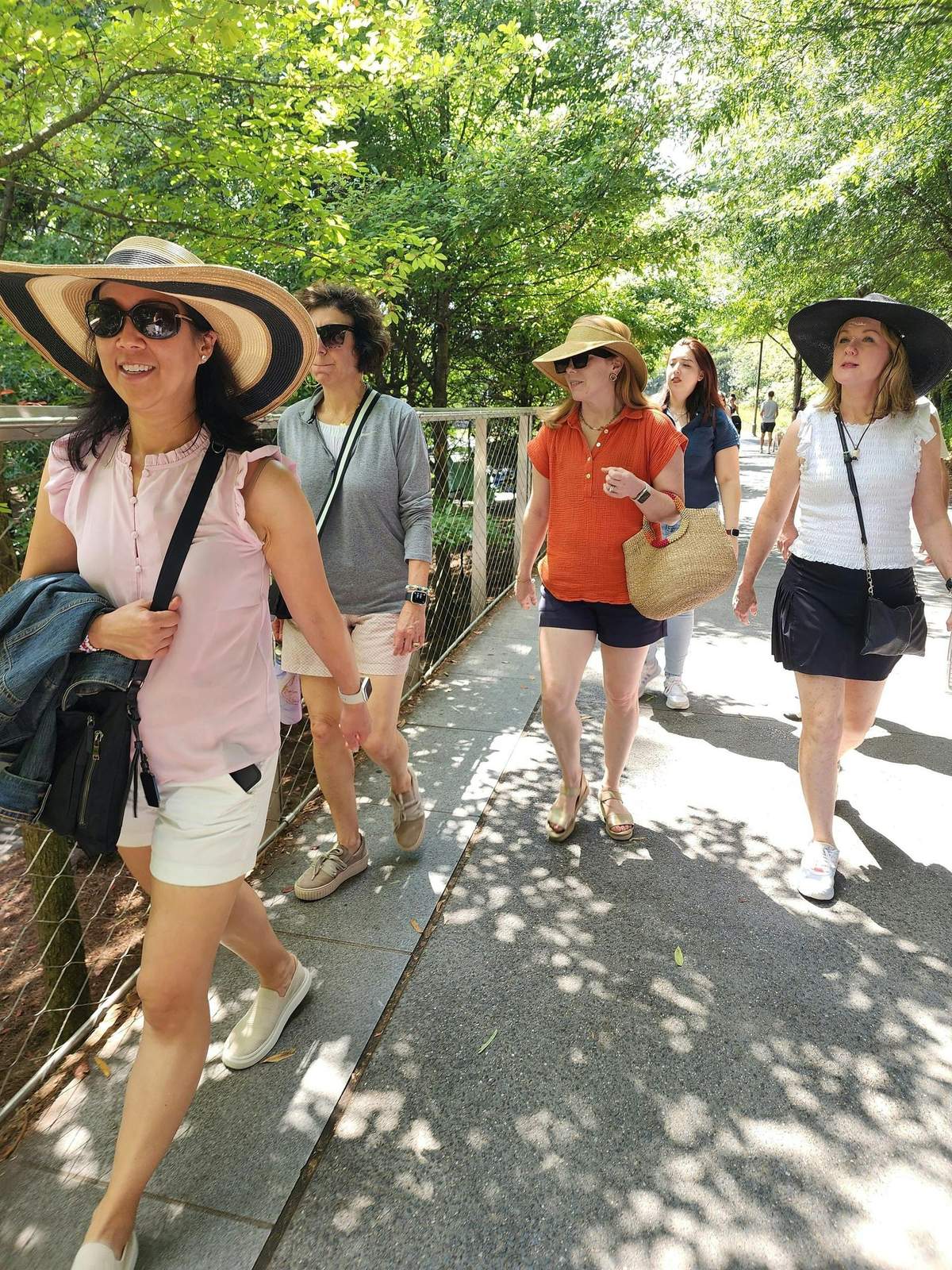 Atlanta Beltline: Food & Street Art Walking Tour A group of women walking outdoors on a sunny day, surrounded by greenery, wearing summer clothes, hats, and sunglasses.