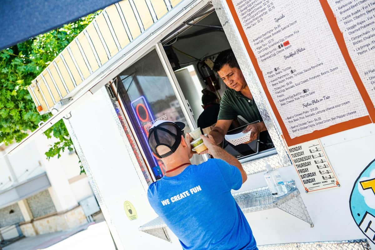 Street Art & Street Food Tour A man in a blue shirt picks up food from a vendor at a food truck with a visible menu and an open service window.