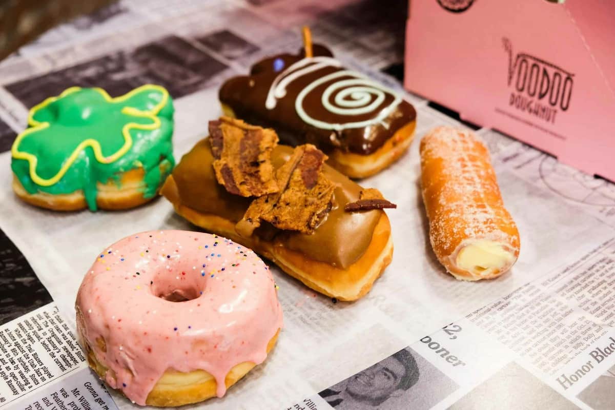 Chicago : Visite guidée du marché Fulton Cinq beignets assortis avec diverses garnitures, dont le glaçage rose, le bacon, le tourbillon de chocolat, le glaçage vert et le fourrage à la crème sur un journal.