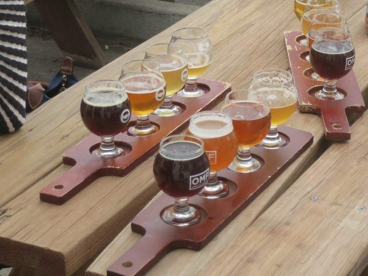 Wooden tables with flights of beer in small glasses arranged on wooden paddles, each containing different beer types.