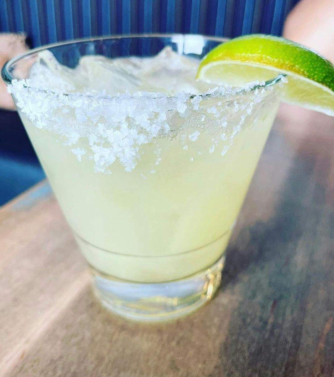 Une margarita avec un bord salé et un quartier de citron vert, servie dans un verre bas sur une table en bois.