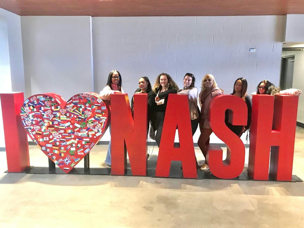 Un groupe de personnes se tenant derrière de grandes lettres rouges formant le mot « NASH », avec à gauche un cœur orné de drapeaux.