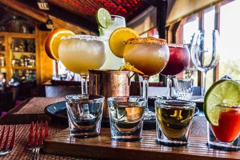 San Diego: Old Town Tales, Tacos and Tequila Walking Tour A variety of colorful cocktails and shots on a wooden board inside a dimly lit bar or restaurant.