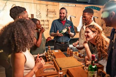 A group of people enjoying a whiskey-tasting session at a distillery, with a presenter holding a bottle of Jameson.