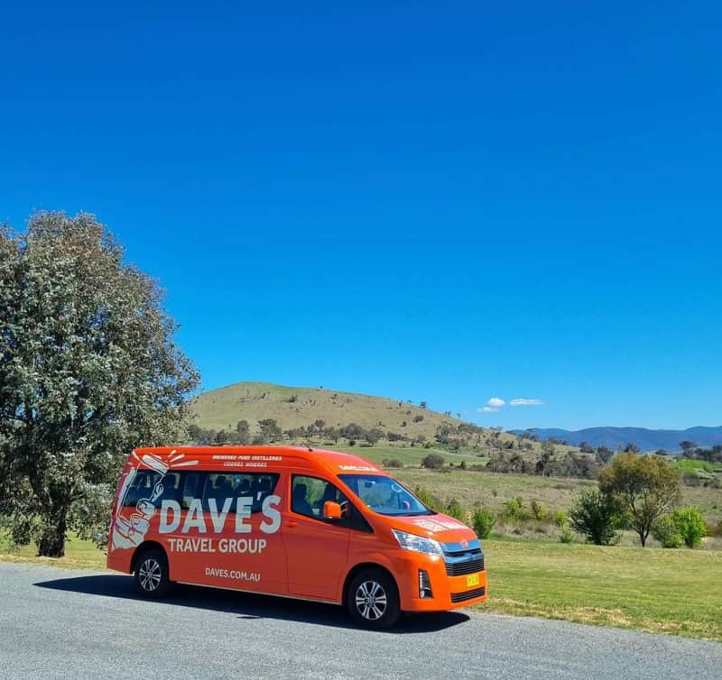 Hunter Valley: Guided Wine Tour from Newcastle + Lunch + Tastings An orange van with 'Dave's Travel Group' branding parked on a roadside, with a scenic countryside landscape in the background.