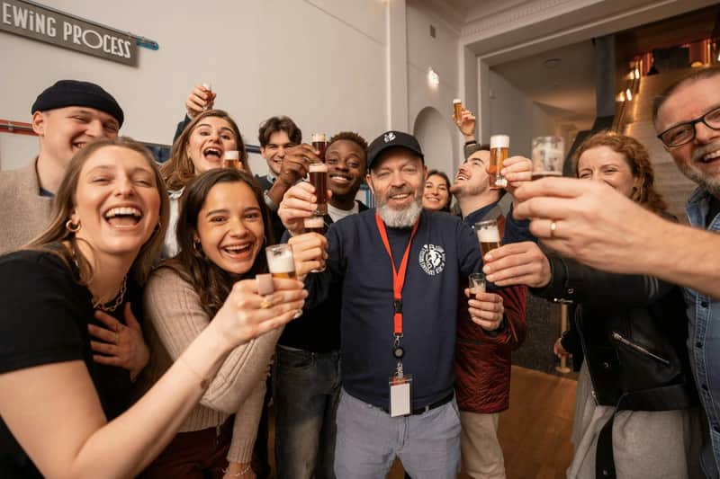 A group of people smiling and holding small glasses together in a celebratory toast in an indoor setting.
