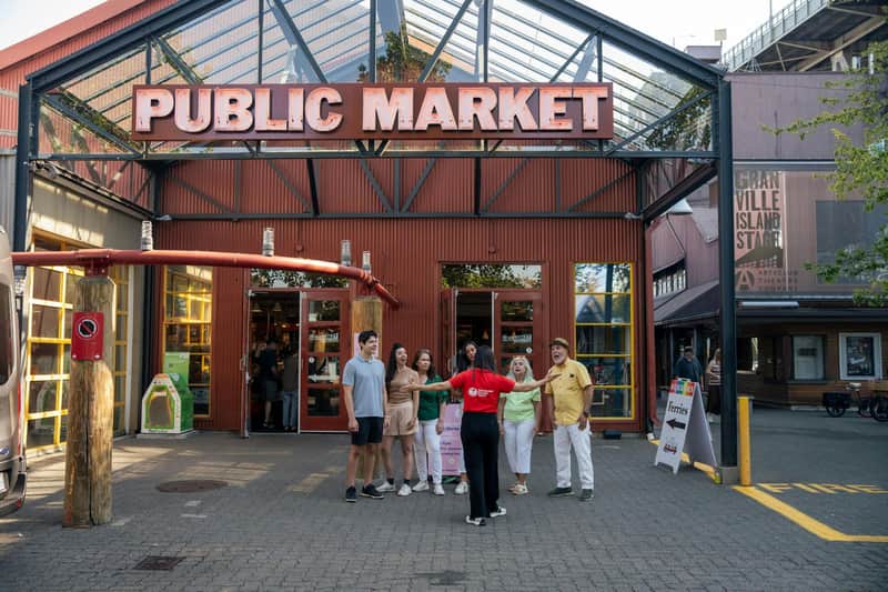 A group of people stands outside a red building with a sign that reads "Public Market." An open doorway and various signs are visible.
