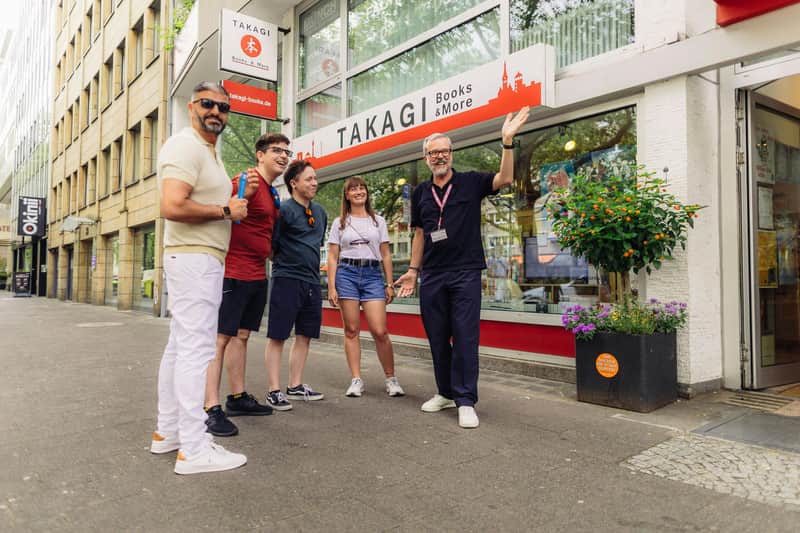 A group of five people standing outside a bookstore named Takagi Books & More on a city street.