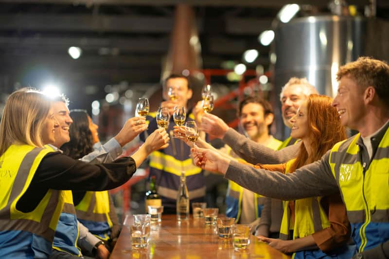 A group of people in safety vests clinking glasses together in a celebratory toast, standing around a wooden table indoors.