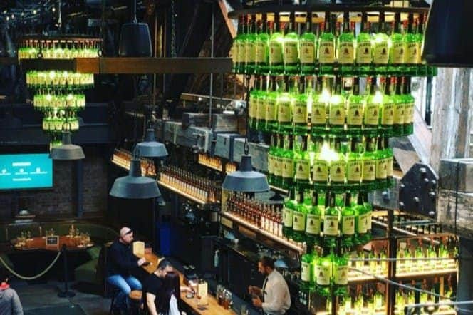 Eine Bar mit einer bis zur Decke reichenden Auslage von Jameson-Whiskey-Flaschen und sitzenden Gästen, die sich mit dem Barkeeper unterhalten.