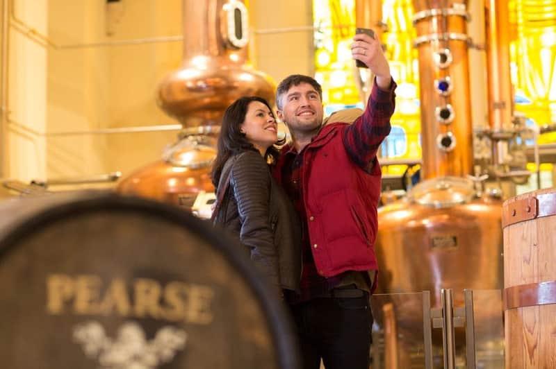 Pearse Lyons Distillery: Guided Tour with 6 Tastings A smiling couple takes a selfie in front of large copper distillery tanks with stained glass in the background.