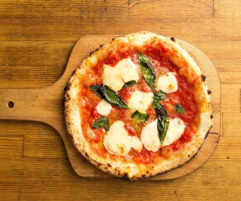 A margherita pizza on a wooden paddle, topped with tomato sauce, melted mozzarella, and fresh basil leaves.