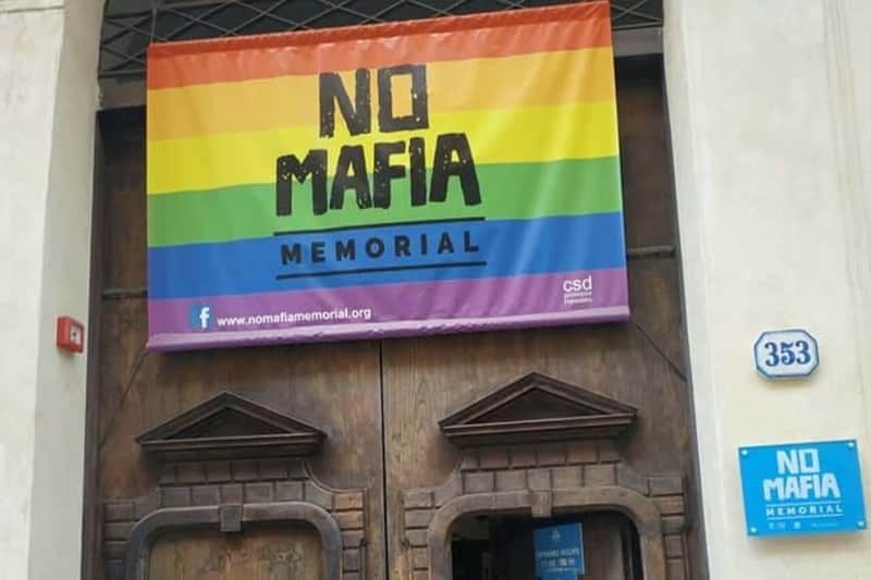 Colorful "No Mafia Memorial" banner above a wooden door, featuring a rainbow design and the website nomafiamemorial.org.