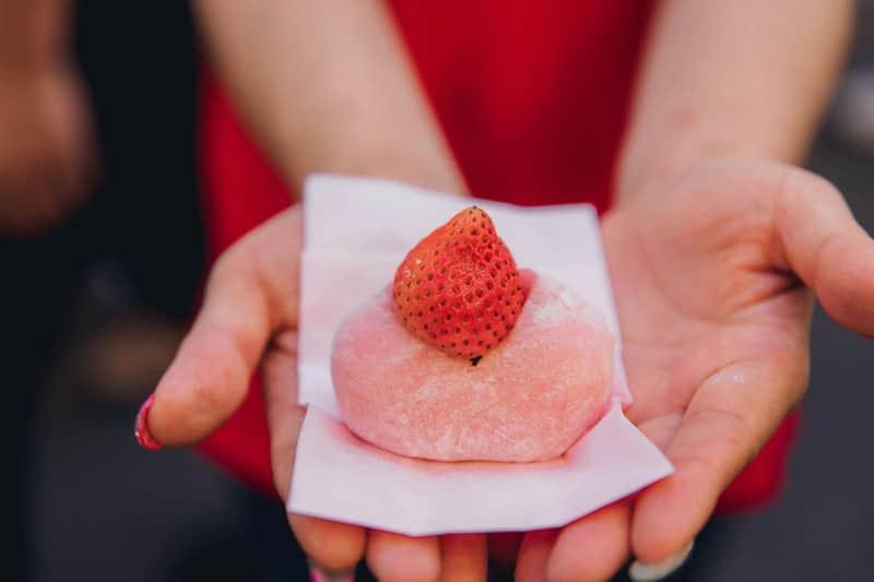 Tokyo: Tour gastronomico in piccolo gruppo al Mercato Esterno di Tsukiji + degustazioni + visita al santuario (Tokyo) Una persona che tiene in mano un mochi rosa con sopra una fragola fresca, su un foglio di carta bianca.