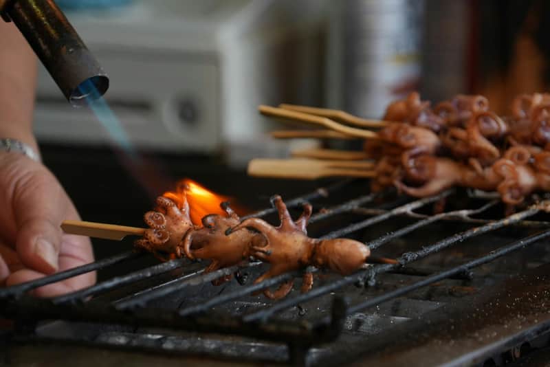 Tsukiji Fish Market: 2-Hr Food & Walking Tour Small octopuses on skewers being grilled over an open flame on a metal grate.