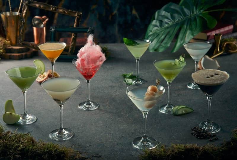 Drinks of Singapore Tour A variety of colorful cocktails in martini glasses on a gray surface with tropical leaves in the background.
