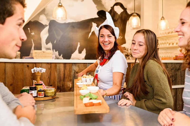 A woman and a girl at a counter with wooden boards of food, cow mural in the background, and hanging pendant lights above.