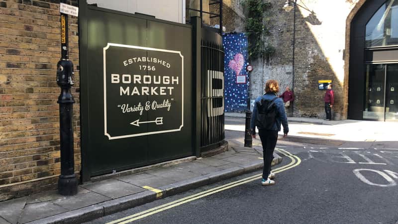 A person walks past a green sign for Borough Market, with surrounding buildings and bystanders in the background.