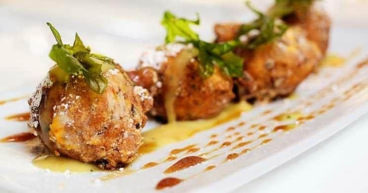 Gros plan sur des beignets garnis de légumes verts et de sauce, présentés sur une assiette blanche.