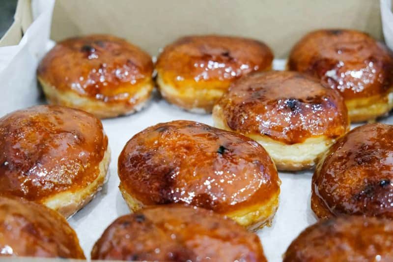 Glazed apple fritters arranged in rows on a white paper-lined surface.